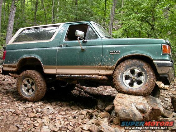 Green 1990 Ford Bronco with tan trim, off-roading over rocks