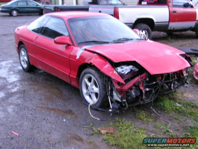 1994 Ford Probe with significant front-end damage, parked on gravel