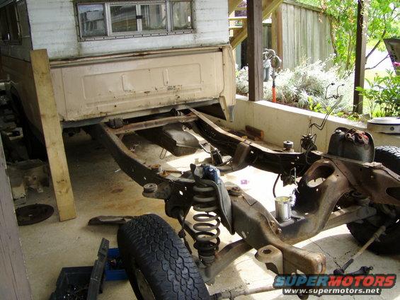Truck chassis with camper shell, disassembled, showing frame and suspension components. Light tan color