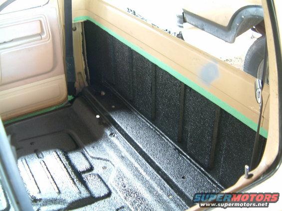 Truck bed interior with black spray-on liner and green masking tape
