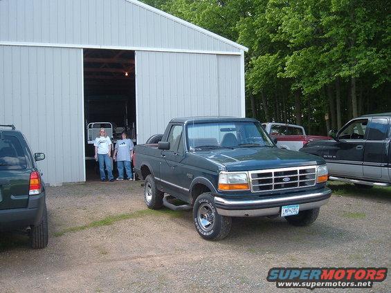 Dark green Ford Bronco with a chrome grille and orange turn signals, parked on a gravel lot
