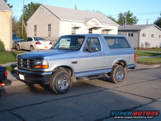1996 Ford Bronco parked on a residential street, showing its side and front quarter. Two-tone blue and silver paint