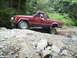 1985 Ford F-150 - A red 1986 Jeep Comanche pickup truck tackles a challenging rocky terrain on an off-road trail.