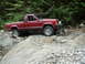 1985 Ford F-150 - Jeep Comanche pickup truck on a challenging rocky trail with dense forest in the background.