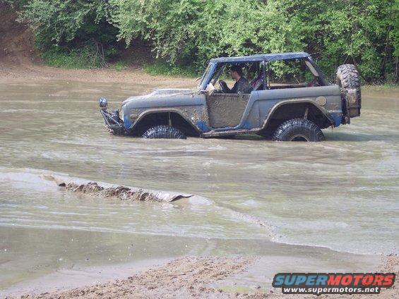 Blue Ford Bronco driving through muddy water, tires submerged