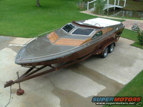Brown boat with wood accents on a dual-axle trailer parked on a concrete driveway