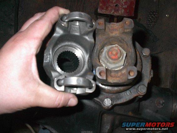 Hand holding new driveshaft U-joint next to old rusty one