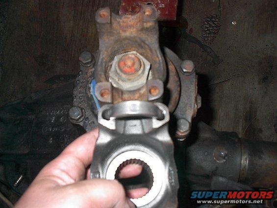 Close-up of a driveshaft U-joint being held near a rusty differential housing