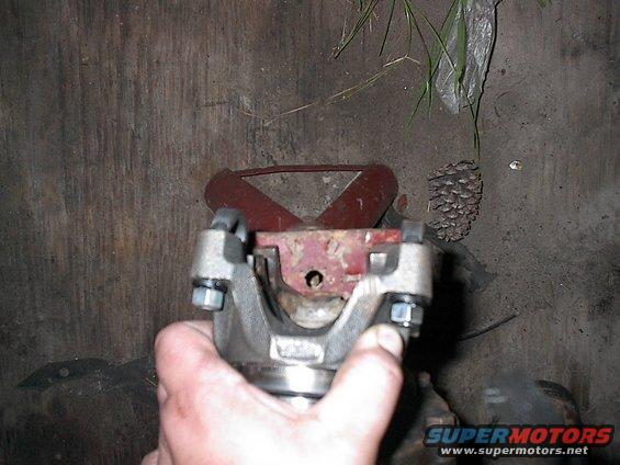 Driveshaft U-joint held by hand, red metal support in background