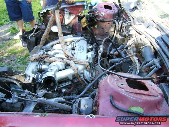 Engine bay of a car with the engine partially removed, showing wiring and structural components