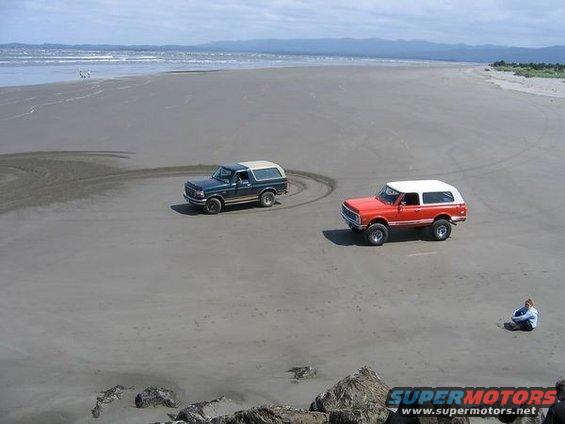 Red and blue SUVs on a sandy beach with ocean in background