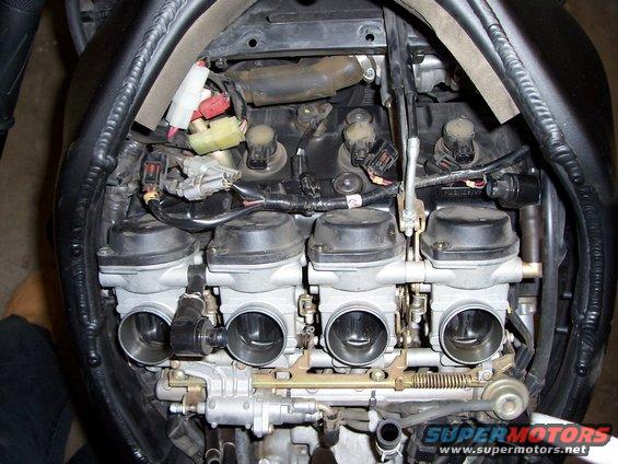 Close-up of a motorcycle's four-cylinder carburetor assembly with wiring and hoses