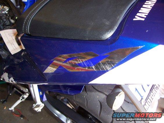 Blue motorcycle fairing with a scratched 'R1' decal and 'YAMAHA' text. A license plate is partially visible
