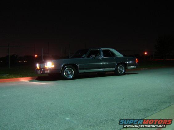 Dark sedan with a white roof, parked at night. Headlights are on