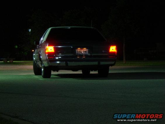 Dark sedan rear view at night, license plate 594 PMF, chrome bumper, red taillights illuminated