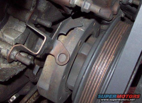 Close-up of a car engine's ribbed pulley and belt, with some mounting brackets visible