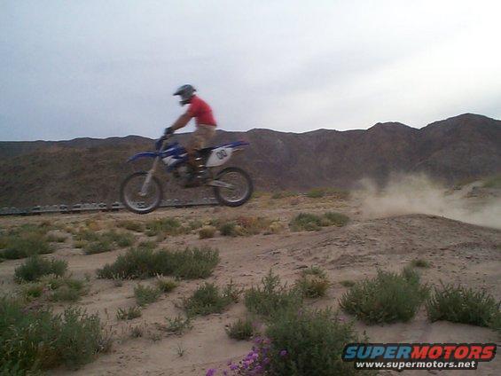 Blue dirt bike jumping in a desert landscape. Number 00 visible on rear fender