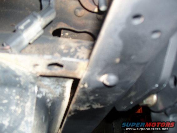 Close-up of vehicle frame and suspension parts, showing rust and bolts