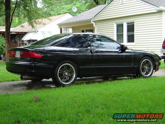 Black 1994 Ford Probe parked on a wet driveway next to a house