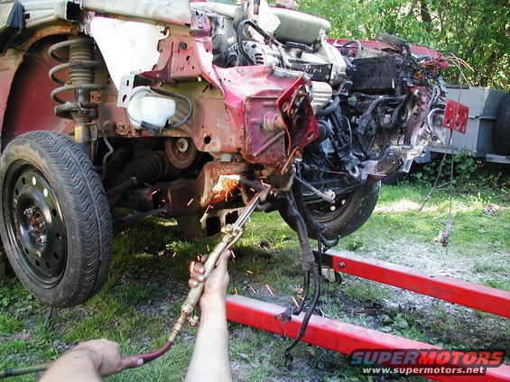 Red car front end being cut with a torch, showing engine and suspension components