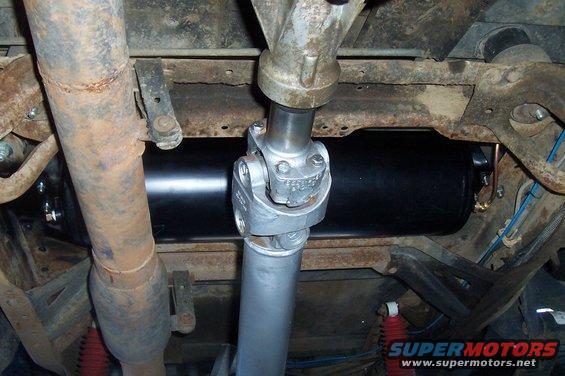 Underside view of a driveshaft and a black air tank mounted to a vehicle frame