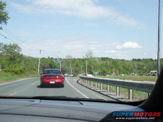Red sedan driving on a highway, seen from behind