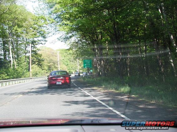 Red 1992 Ford Taurus driving on a highway, rear view, trees line the road
