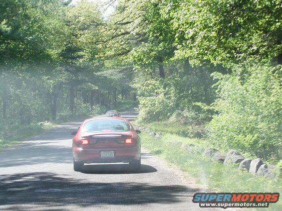 Red sedan with a spoiler, seen from behind on a tree-lined road
