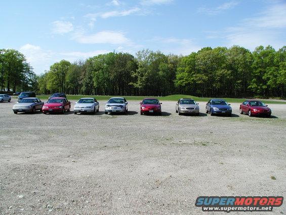 Several sedans parked in a gravel lot with trees in the background
