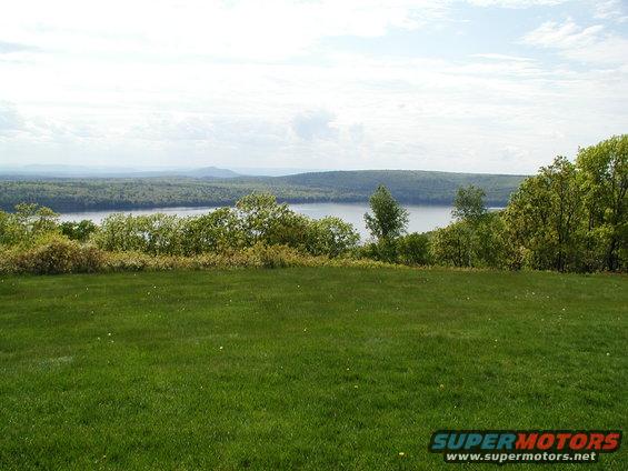 Grassy hill overlooking a lake and forested hills under a cloudy sky