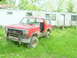 1984 Ford Bronco - This red 1980s Ford Bronco, a brush guard, sits in overgrown grass beside a trailer.
