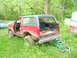 1984 Ford Bronco - This red Ford Bronco appears to be in disrepair, with its doors removed and body panels showing significant damage.