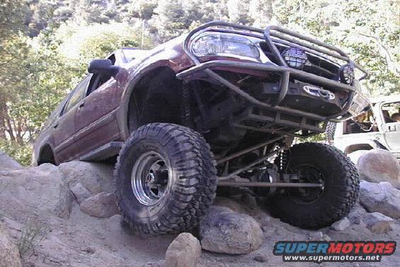 Maroon 1997 Ford Ranger off-roading on rocks, lifted with large tires and custom bumper
