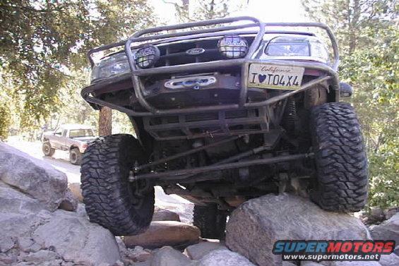 Red Ford Ranger with custom roll cage and winch, front view, on rocks