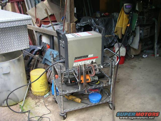 Welding machine on a cart with tools and a yellow bucket nearby in a cluttered garage