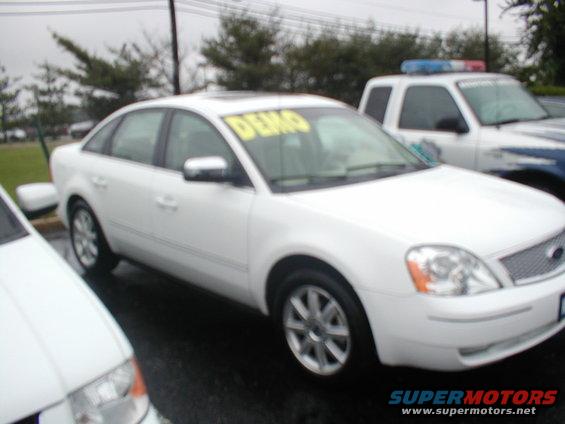 White sedan with yellow DEMO sign on windshield parked next to police SUV
