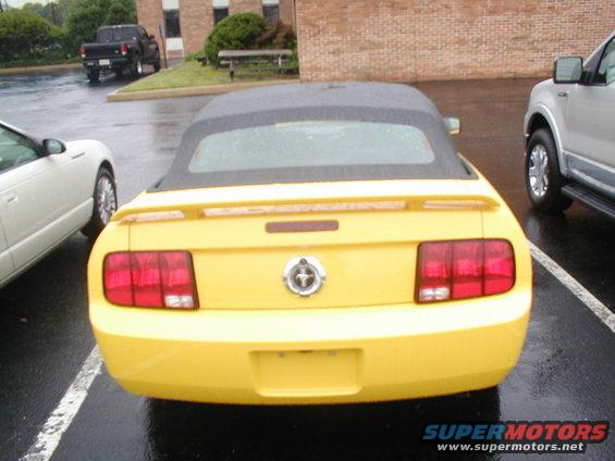 Yellow convertible car's rear end, parked in a lot with other vehicles and a brick building