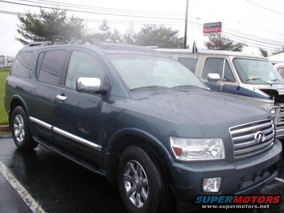 Dark green SUV parked on a wet asphalt lot, with a blue and white van behind it