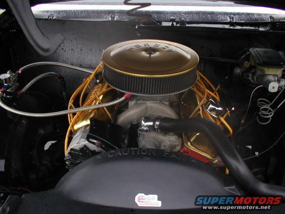 Engine bay with gold air cleaner and gold valve covers. "CAUTION FAN" text visible