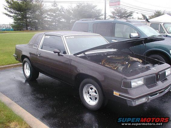 Dark brown 1981 Oldsmobile Cutlass coupe with hood open, parked next to a dark green SUV