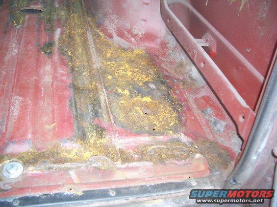 rusted red floor pan with yellow and black discoloration, showing metal fatigue and holes