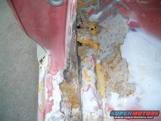 Close-up of a red metal panel with significant rust and peeling paint, showing exposed metal and primer