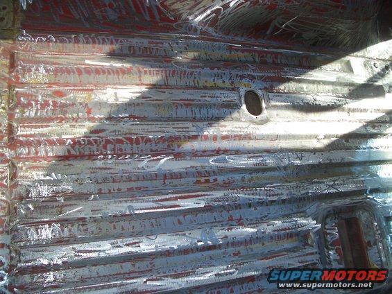 Corrugated metal floor pan with red primer and white paint scraped off