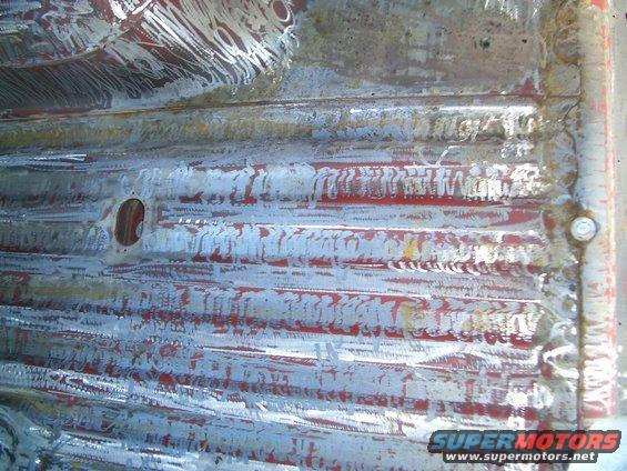 Corrugated metal floor with red paint and white primer residue, showing weld marks and a circular cutout