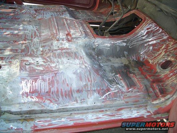 Interior floor pan stripped and prepped for repair, showing red primer and metal