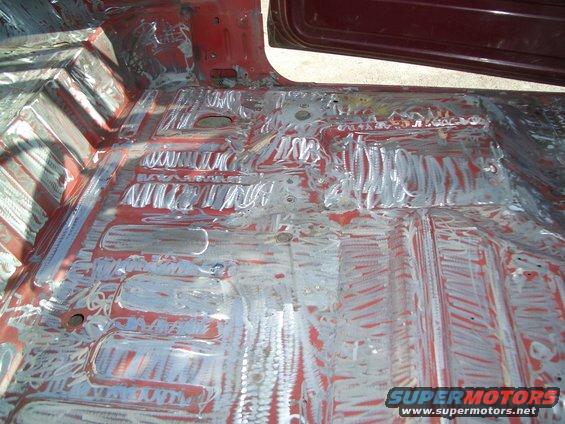 Car floor stripped down, showing red primer and metal with grinding marks
