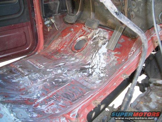 Red interior floor with exposed metal and white residue, showing pedals and door frame