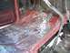 1981 Ford Bronco - The interior floor of a vehicle shows exposed metal and red paint, with pedals visible.
