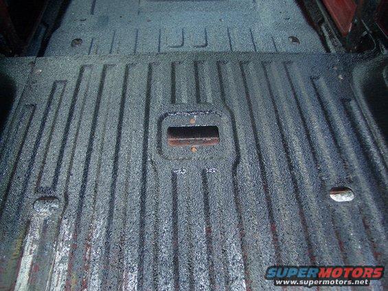 Truck bed floor with ribbed texture and a metal tie-down point