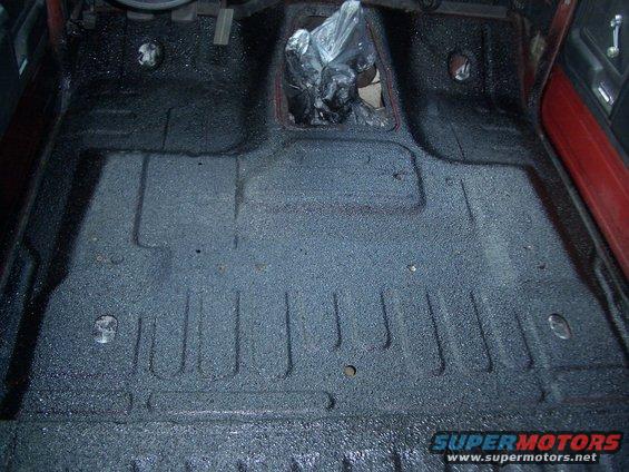 Black textured floor of a vehicle interior with plastic-wrapped shifter area